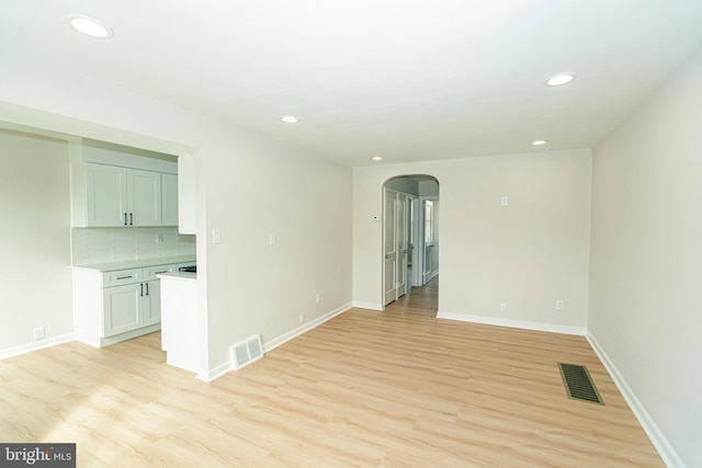 unfurnished room with arched walkways, visible vents, light wood-style flooring, and baseboards