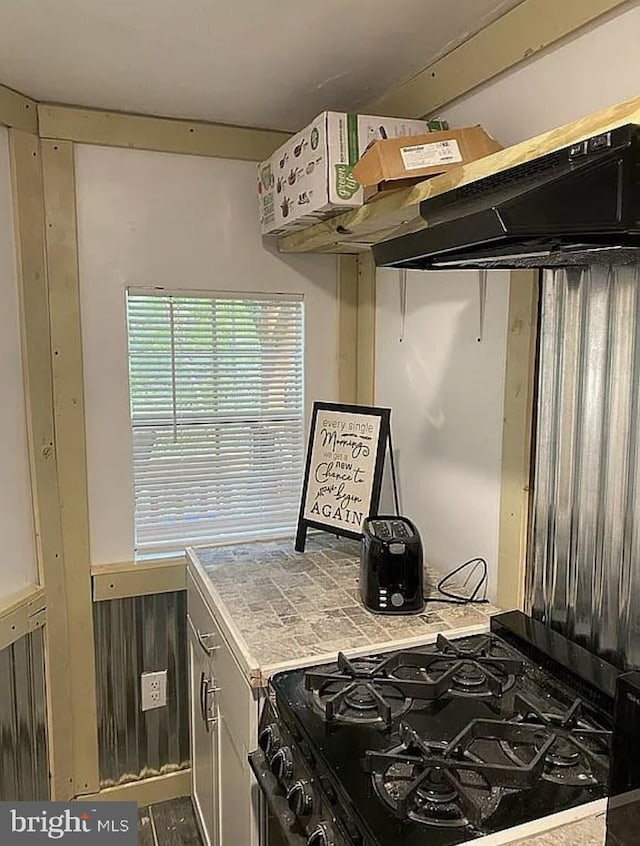 kitchen featuring black gas range oven, wooden walls, and tile countertops