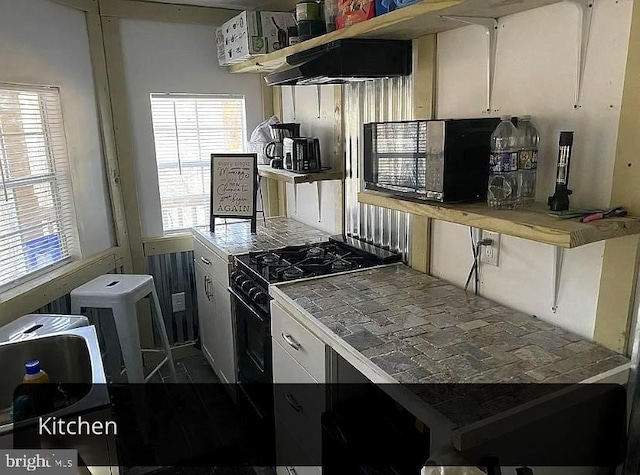 kitchen with under cabinet range hood, white cabinets, black gas stove, and tile countertops