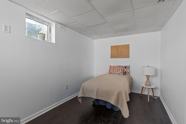 bedroom featuring a drop ceiling, baseboards, and wood finished floors