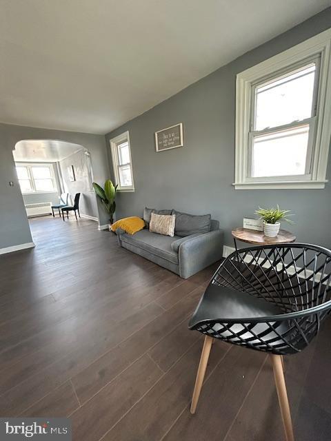 living area featuring arched walkways, dark wood-type flooring, and baseboards