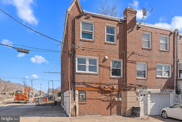 townhome / multi-family property with driveway, brick siding, a chimney, and an attached garage