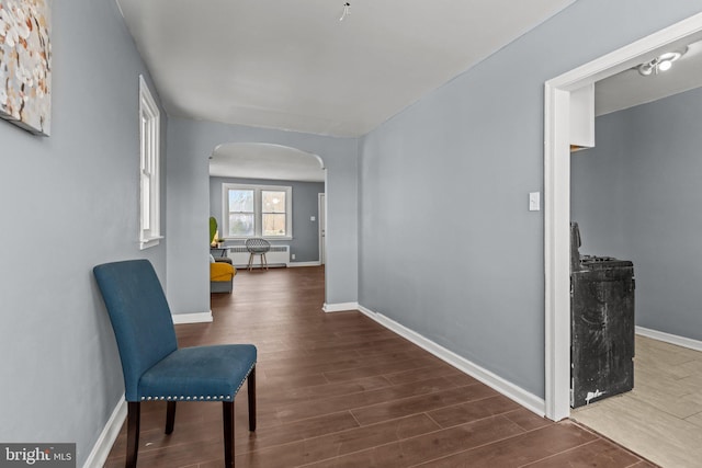 corridor with arched walkways, baseboards, and wood finished floors