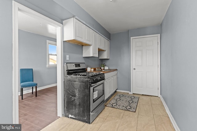 kitchen with gas range, white cabinetry, and baseboards