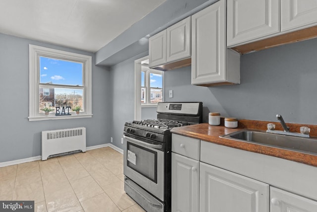 kitchen featuring stainless steel gas range oven, a sink, white cabinetry, radiator, and baseboards