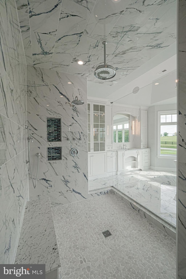 bathroom featuring a marble finish shower, vanity, and tile walls