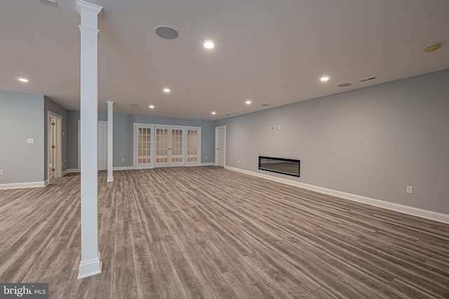 unfurnished living room featuring wood finished floors, a glass covered fireplace, decorative columns, and baseboards