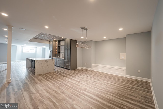 unfurnished living room with recessed lighting, light wood-style floors, a sink, wet bar, and baseboards