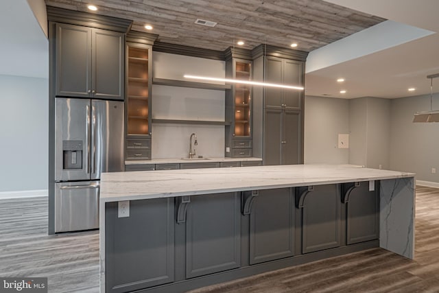 kitchen with gray cabinetry, wood finished floors, a sink, stainless steel fridge with ice dispenser, and light stone countertops