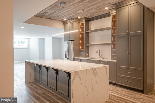 kitchen featuring light stone counters, a sink, wood finished floors, a center island, and stainless steel fridge