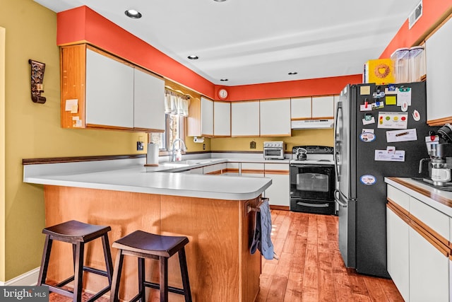 kitchen with a peninsula, freestanding refrigerator, white cabinets, electric stove, and under cabinet range hood