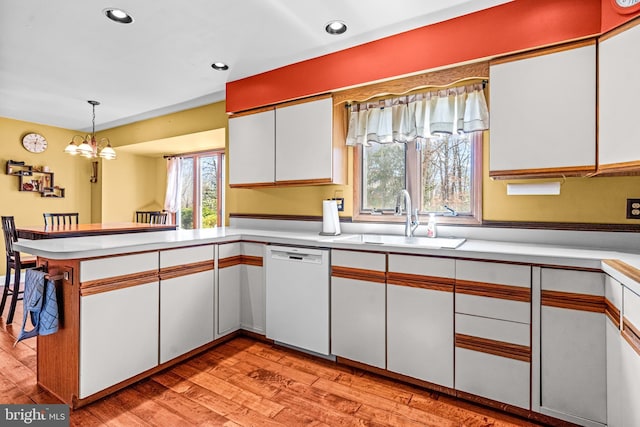 kitchen featuring light wood-style flooring, a peninsula, white dishwasher, white cabinetry, and a sink