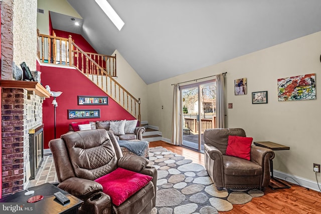 living area with high vaulted ceiling, wood finished floors, stairway, a skylight, and a brick fireplace