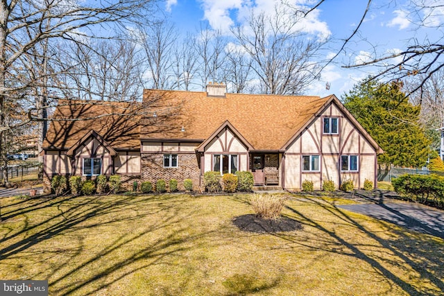 english style home with roof with shingles, a chimney, a front lawn, and fence