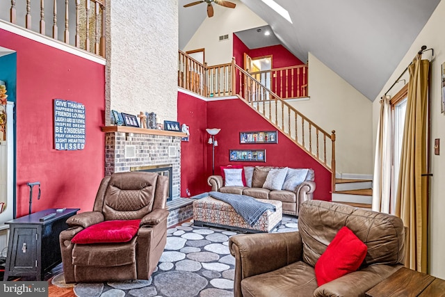 living room with ceiling fan, stairway, a fireplace, wood finished floors, and high vaulted ceiling