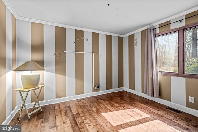 unfurnished room with visible vents, wallpapered walls, crown molding, baseboards, and hardwood / wood-style flooring