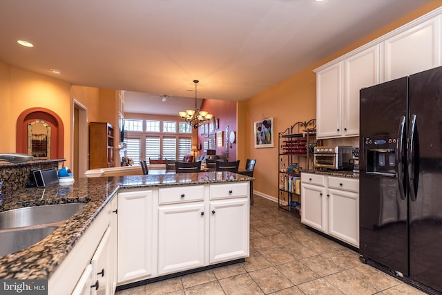 kitchen with dark stone countertops, a chandelier, white cabinets, and black fridge