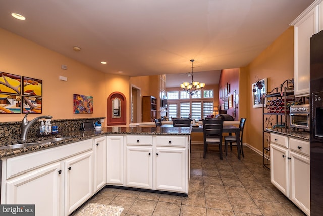 kitchen with decorative light fixtures, an inviting chandelier, white cabinetry, a sink, and dark stone countertops