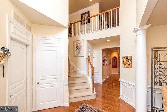 entryway featuring light wood-style flooring, a towering ceiling, visible vents, stairs, and decorative columns