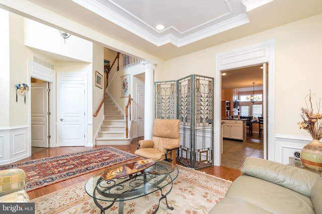 living area with a chandelier, wainscoting, crown molding, and stairway