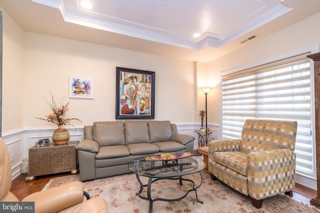 living area with ornamental molding, a raised ceiling, wainscoting, and wood finished floors