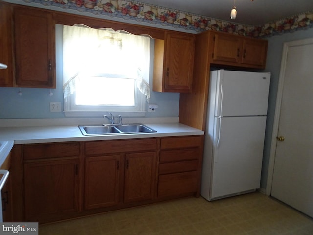 kitchen with a sink, light floors, brown cabinetry, and freestanding refrigerator