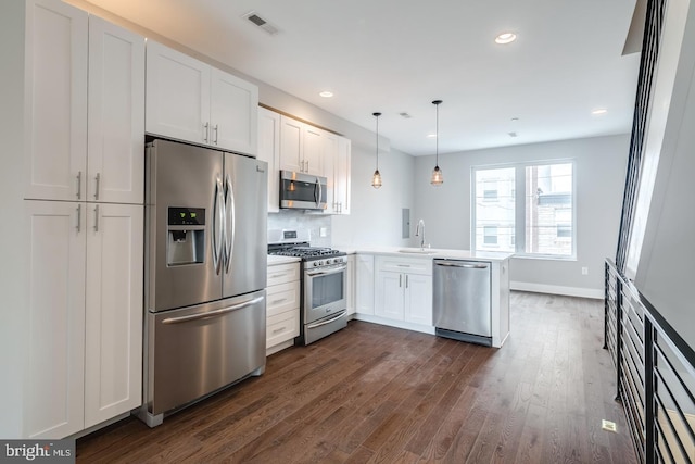 kitchen featuring stainless steel appliances, dark wood-type flooring, white cabinets, a sink, and a peninsula