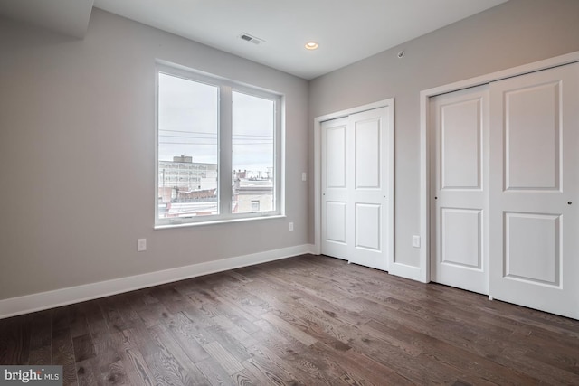 unfurnished bedroom with baseboards, dark wood-style floors, visible vents, and multiple closets