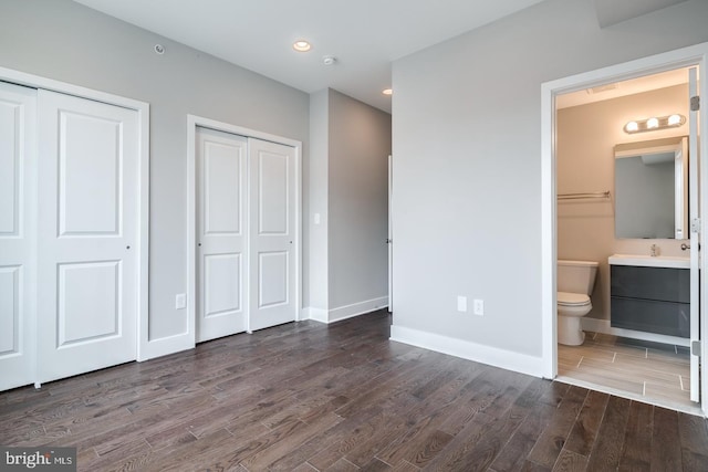 unfurnished bedroom with multiple closets, recessed lighting, connected bathroom, wood finished floors, and baseboards