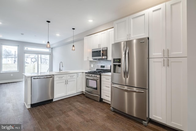 kitchen featuring stainless steel appliances, dark wood-type flooring, white cabinetry, a sink, and a peninsula