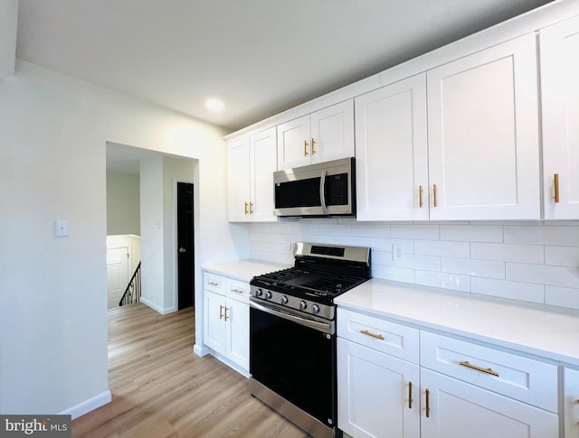 kitchen featuring light wood finished floors, tasteful backsplash, baseboards, white cabinets, and appliances with stainless steel finishes