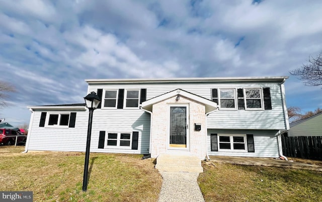 raised ranch featuring fence and a front lawn