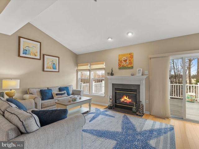 living area with visible vents, baseboards, lofted ceiling, a fireplace with flush hearth, and light wood-style floors