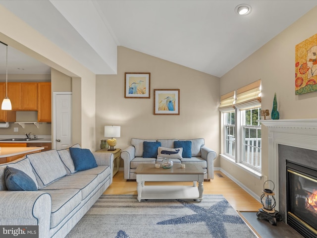 living room with light wood-style floors, baseboards, vaulted ceiling, and a glass covered fireplace