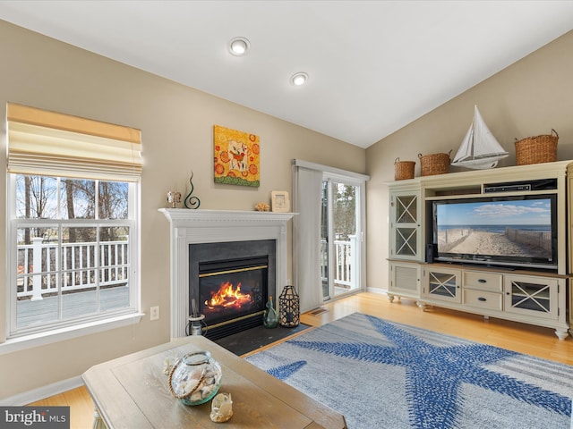 living room with lofted ceiling, light wood-style flooring, a fireplace with flush hearth, and a wealth of natural light