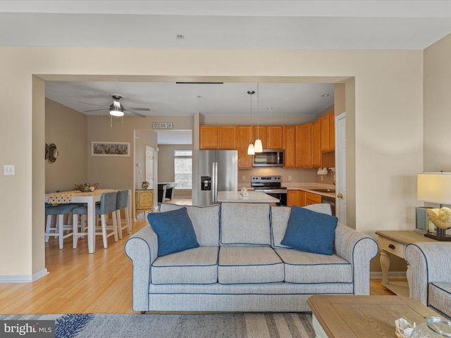 living area with baseboards, a ceiling fan, and light wood-style floors