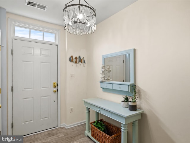 foyer with visible vents, a notable chandelier, baseboards, and wood finished floors