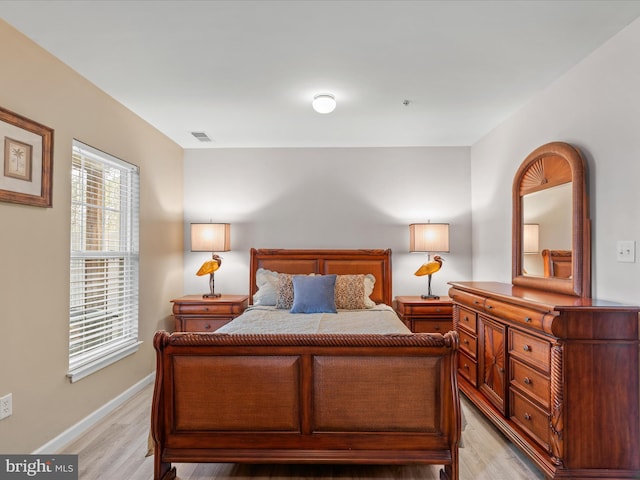 bedroom with light wood finished floors, visible vents, and baseboards