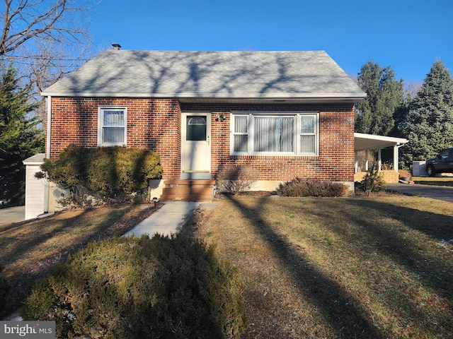 view of front facade featuring roof with shingles, a front yard, an attached carport, and brick siding