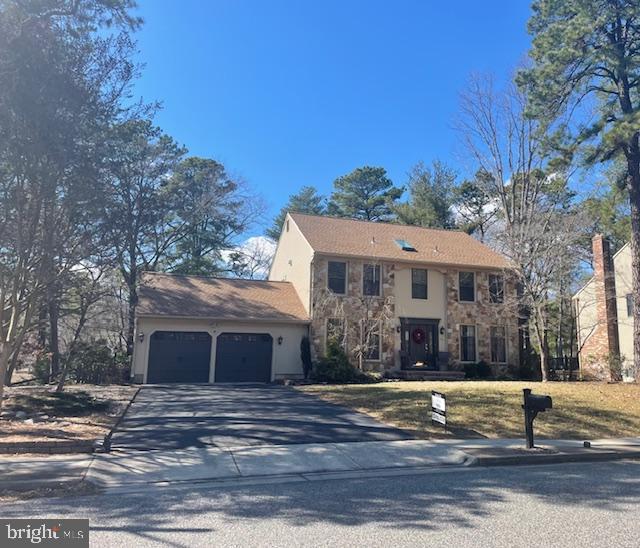 colonial-style house with a garage, stone siding, and concrete driveway