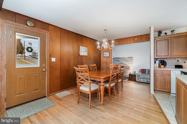 dining area with light wood-style floors, a notable chandelier, and wood walls