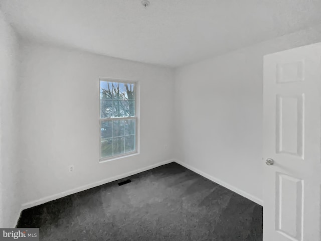 spare room featuring visible vents, dark carpet, and baseboards