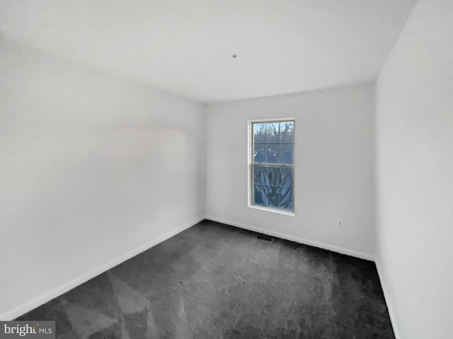 unfurnished room featuring dark colored carpet, visible vents, and baseboards