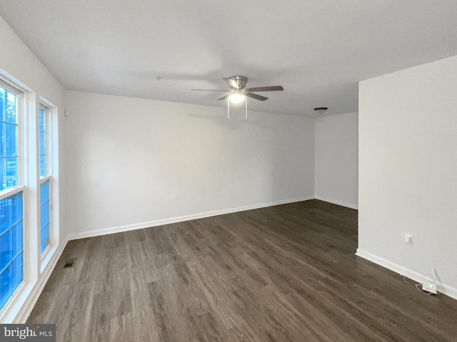 empty room with dark wood-style floors, visible vents, a ceiling fan, and baseboards