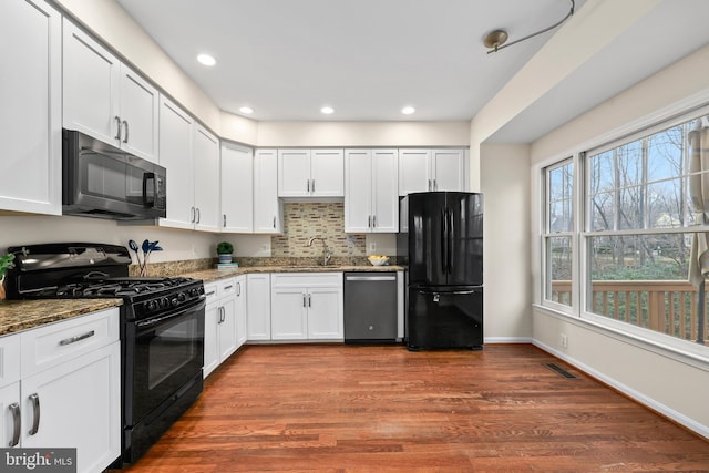 kitchen featuring dark stone countertops, white cabinets, black appliances, and wood finished floors