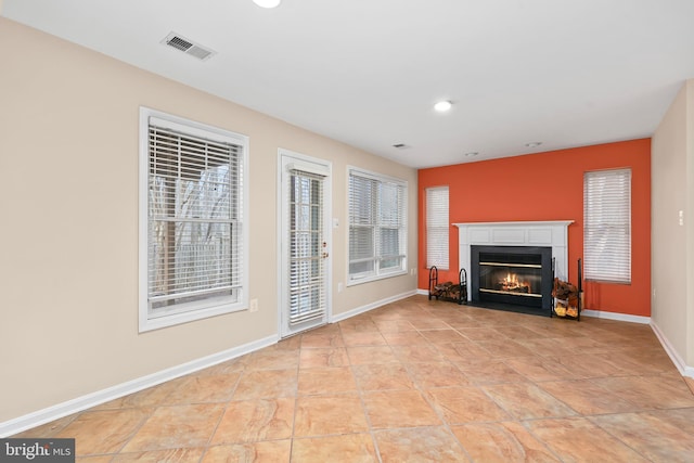 unfurnished living room featuring visible vents, baseboards, a healthy amount of sunlight, and a fireplace with flush hearth