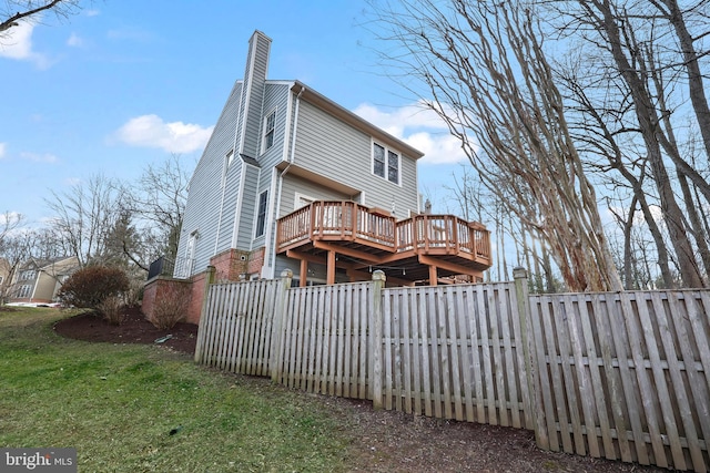 back of house featuring a chimney, a lawn, a wooden deck, and fence