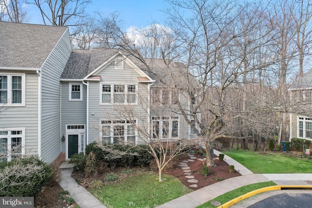 multi unit property with uncovered parking, a front yard, and roof with shingles