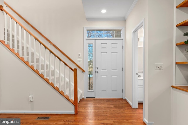 foyer with visible vents, baseboards, stairs, ornamental molding, and wood finished floors