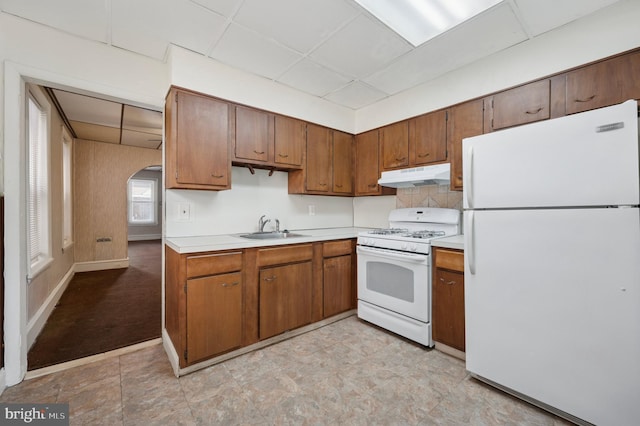 kitchen with under cabinet range hood, light countertops, arched walkways, white appliances, and a sink